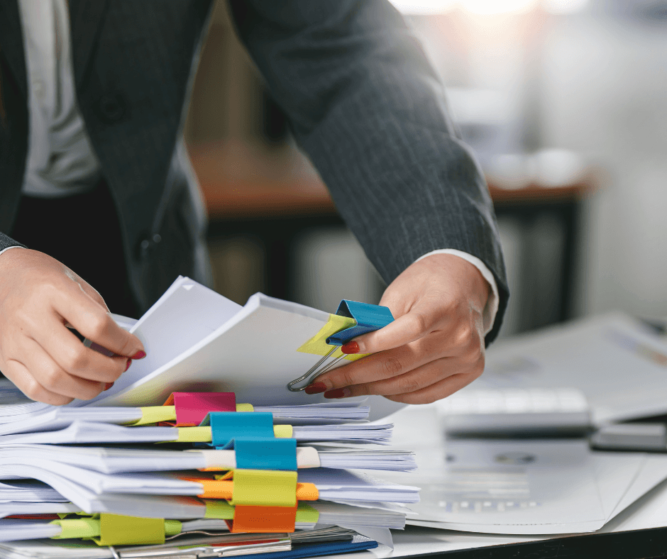 Person organising a stack of paperwork and documents with colourful tabs, illustrating the importance of keeping accurate records for residential rental property management.